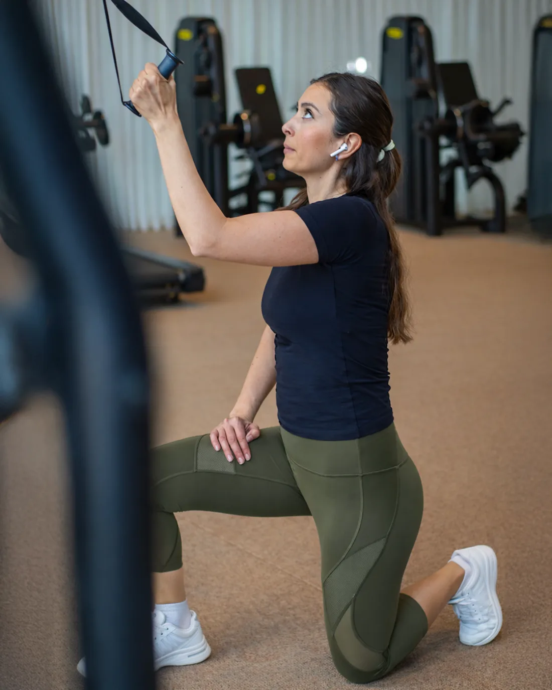 A member kneeling at the functional trainer, drawing a cable handle overhead in the strength studio at Vy Boutique