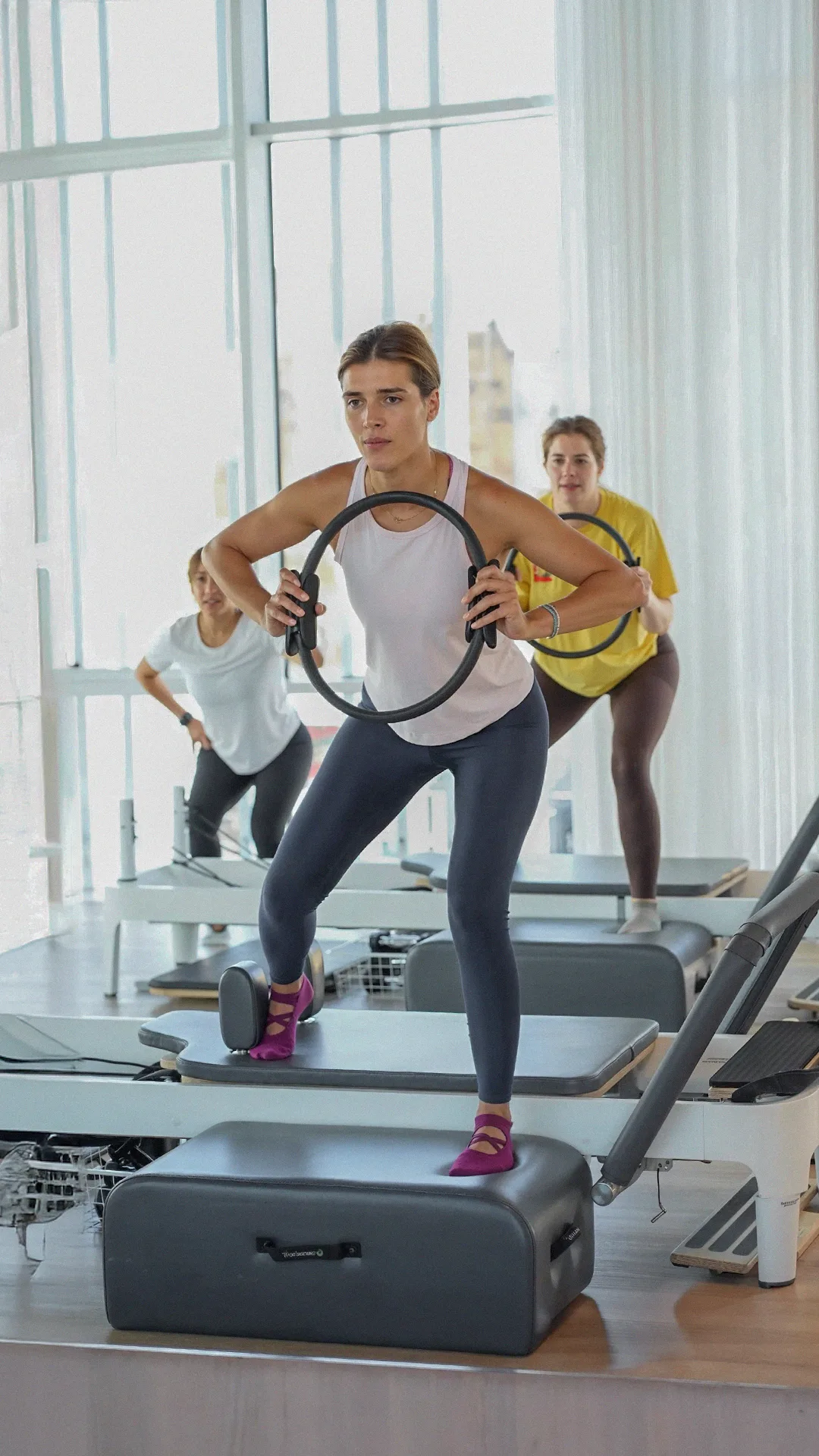 Members training with the Pilates ring on the reformers, daylight through the studio windows
